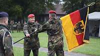 Ein Soldat übernimmt eine Fahne von einem anderen Soldaten.