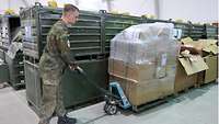 Ein Soldat transportiert in mehreren Kartons übereinandergestapeltes Material in ein Lager 