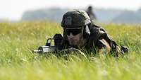 Ein Soldat liegt im Gras und sichert mit seinem Gewehr die Umgebung.