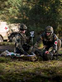 Two medics provide medical care to a casualty in front of a MRAV Boxer