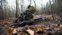 Ein Bundeswehrsoldat gleitet mit dem Gewehr G36 über den Waldboden