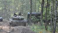 Zwei Soldaten sind auf einem Panzer im Wald und bekommen ihre Verpflegung von einem weiteren Soldaten, der neben einem Lkw steht