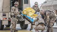 Vier Soldaten transportieren eine Verwundetentrage in ein Rettungsfahrzeug