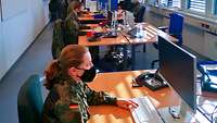 Soldatinnen und Soldaten sitzen in einem Großraumbüro an Bildschirmarbeitsplätzen 