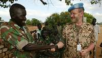 Deutscher Soldat reicht einem nordsudanesischen Kameraden die Hand.