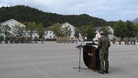 Ein Soldat steht auf einem Appellplatz hinter einem Rednerpult. Vor ihm sind zahlreiche Soldaten angetreten.