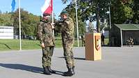 Zwei Soldaten stehen auf einem Appellplatz. Einer gratuliert dem anderen.