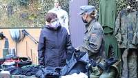Eine Frau in Zivil und eine Soldatin schauen sich Bekleidung und Ausrüstungsgegenstände von Soldaten an