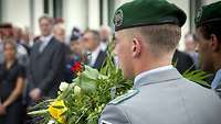 Soldat hält einen Blumenstrauß und steht mit dem Rücken zugewandt