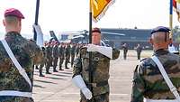 Bei der Kommandoübergabe tragen zwei deutsche Soldaten und ein französischer Soldat jeweils eine Truppenfahne.