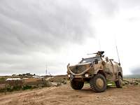 Ein Transportfahrzeug vom Typ Dingo im Gelände, im Hintergrund ein Bundeswehr-Feldlager