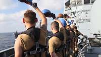 Soldaten stehen an Oberdeck und winken einem anderen Schiff mit ihren blauen Helmen