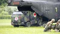 An emergency vehicle of the Medical Service marked with a Red Cross exits the tail section of a helicopter into a field.