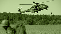 An NH90 helicopter hovers closely above a field.
