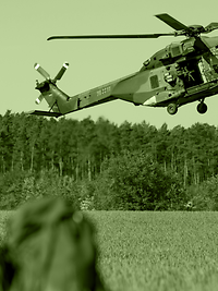 An NH90 helicopter hovers closely above a field.