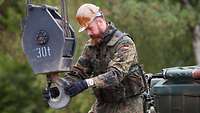 A serviceman controls the crane hook of an armoured recovery vehicle with both hands.