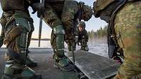 Four soldiers attach a ramp to a metal bridge in ice and snow.