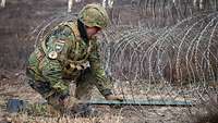Just before demolition: An engineer attaches an explosive charge to a concertina wire obstacle.