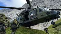 An NH-90 utility helicopter hovers just above the ground to pick up infantry soldiers.