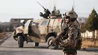 An infantryman provides security during an operation. A Dingo can be seen in the background.