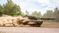 A Leopard 2 MBT traverses dust-clouded open ground.