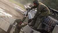 : A soldier standing next to a main battle tank passes ammunition to a comrade atop the tank.