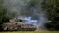 A Puma IFV standing in a meadow fires towards a wooded area.