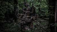 Two soldiers provide mutual cover and security in a dark forest.