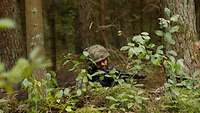 Ein Soldat liegt mit seinem Maschinengewehr in einer getarnten Stellung im Wald