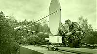 A soldier setting up a satellite antenna on a rooftop.