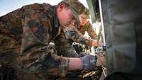 Two soldiers kneeling on the ground, arranging data and power lines.