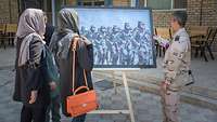 Zwei Frauen und ein niederländischer Soldat betrachten ein Bild mit Frauen bei der afghanischen Armee