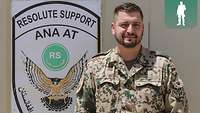 Ein Soldat steht rechts neben dem Wappen des Beraterteams mit der Aufschrift Resolute Support