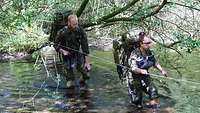 Eine Soldatin und zwei Soldaten waten durch einen Tümpel