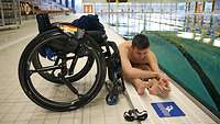 Ein Mann sitzt am Schwimmbeckenrand neben einem Rollstuhl
