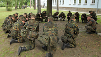 Eine Gruppe von Soldaten knien auf einer Wiese im Kreis und schreiben auf Blöcke. 