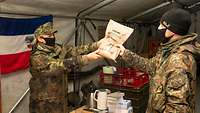 Eine Soldatin reicht einem Kameraden eine Einmannpackung.