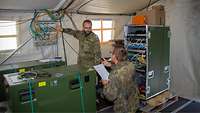 Hauptfeldwebel H. prüft gemeinsam mit einem Soldaten, in einem Zeltaufbau die zuvor installierten Verbindungswege der Kabel