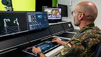 Ein Soldat sitzt vor mehreren Bildschirmen und bedient mit beiden Händen eine Tastatur