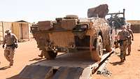 Eine Soldatin und zwei Soldaten laufen in der Wüste um ein verladenes Fahrzeug