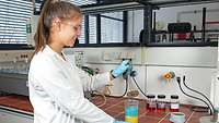 A young woman standing at a work surface mixing two liquids in a glass container