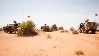 Drei gepanzerte Fahrzeuge stehen in der Wüste Afrikas auf einer Straße.