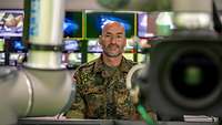 A soldier stands between television cameras in front of numerous monitors