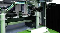 Two mechanical arms with cameras stand on a green floor in a room