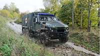 A small truck painted in camouflage pattern is driving through woodland