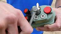 A person holding a green box with red buttons and a crank