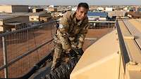 Ein Soldat schraubt einen Belüftungsschlauch ab, im Hintergrund ein Camp in der Wüste