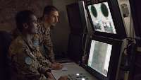 Zwei Soldaten arbeiten vor Monitoren in einem abgedunkelten Raum 