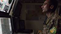 Ein Soldat schaut auf verschiedene Monitore in einem abgedunkelten Raum 