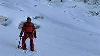 Ein Mann steht auf einem Berg in knöcheltiefem Schnee 